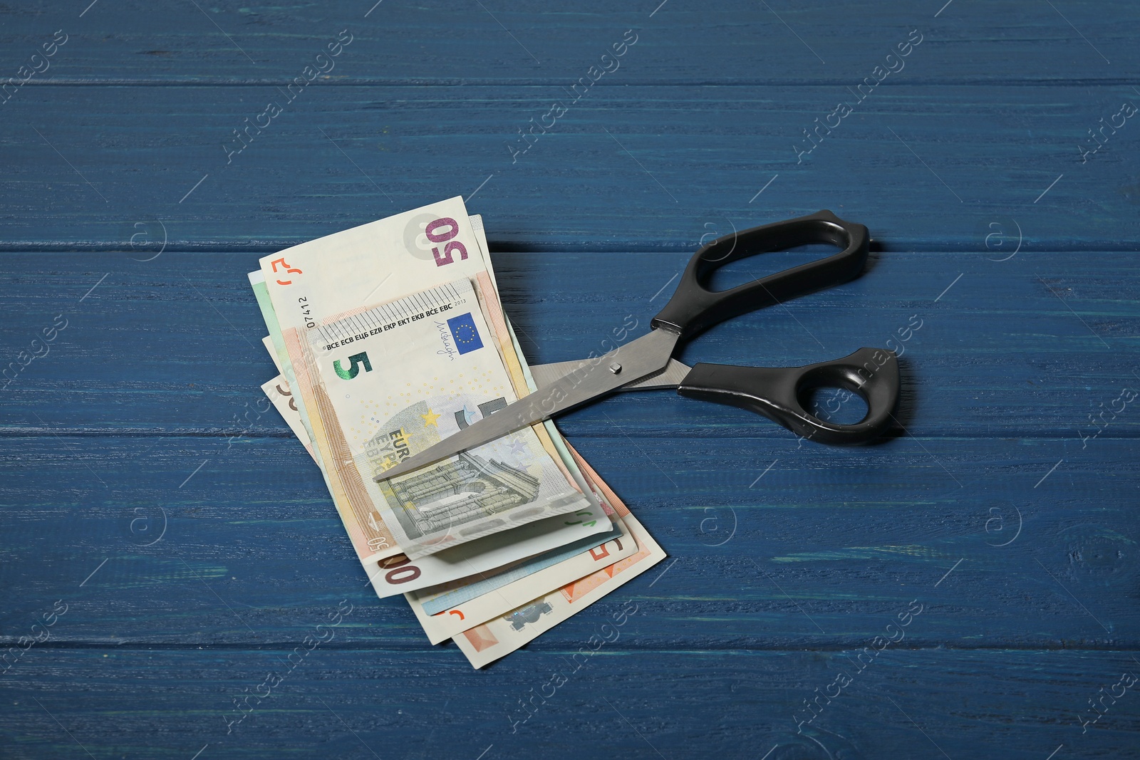 Photo of Euro banknotes and scissors on blue wooden table