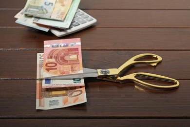 Photo of Euro banknotes, scissors and calculator on wooden table