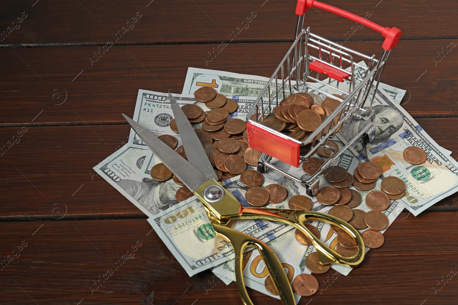 Photo of Dollar banknotes, scissors, coins and small shopping cart on wooden table