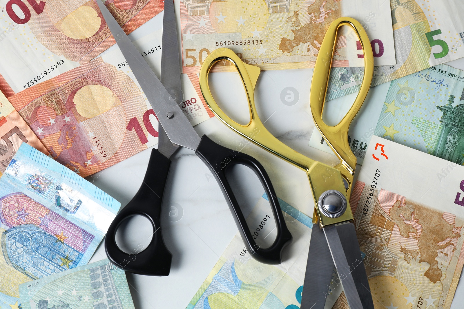 Photo of Euro banknotes and scissors on light marble table, flat lay