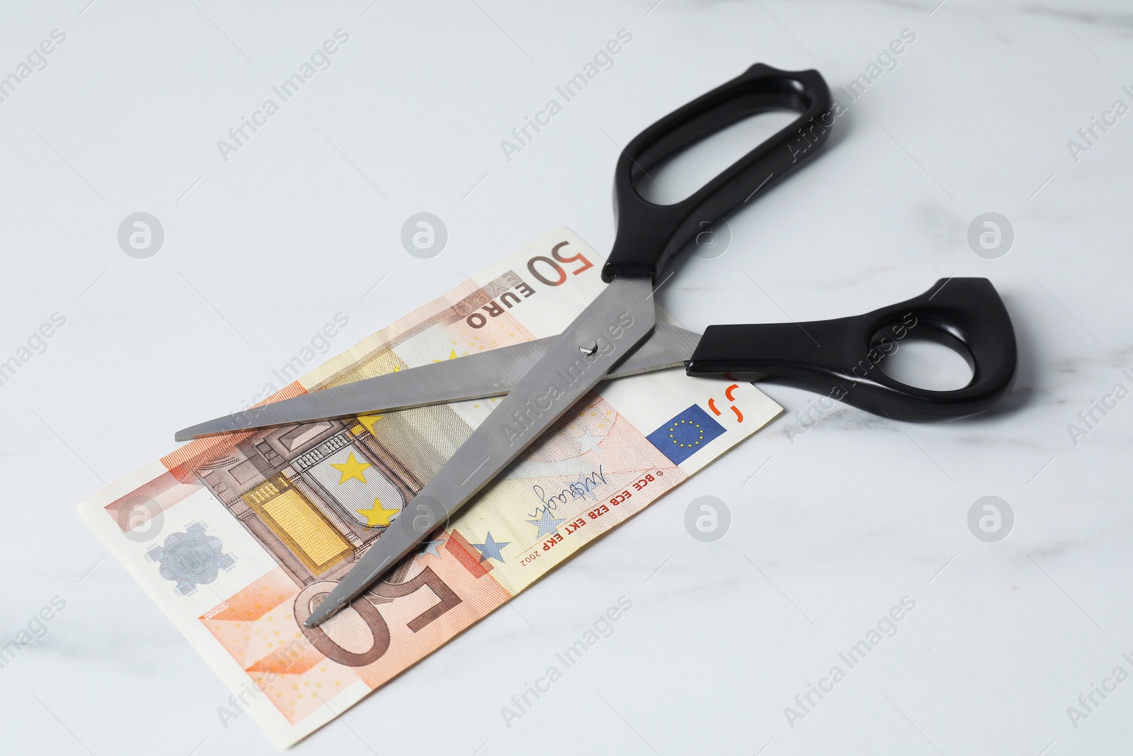 Photo of Euro banknote and scissors on light marble table, closeup