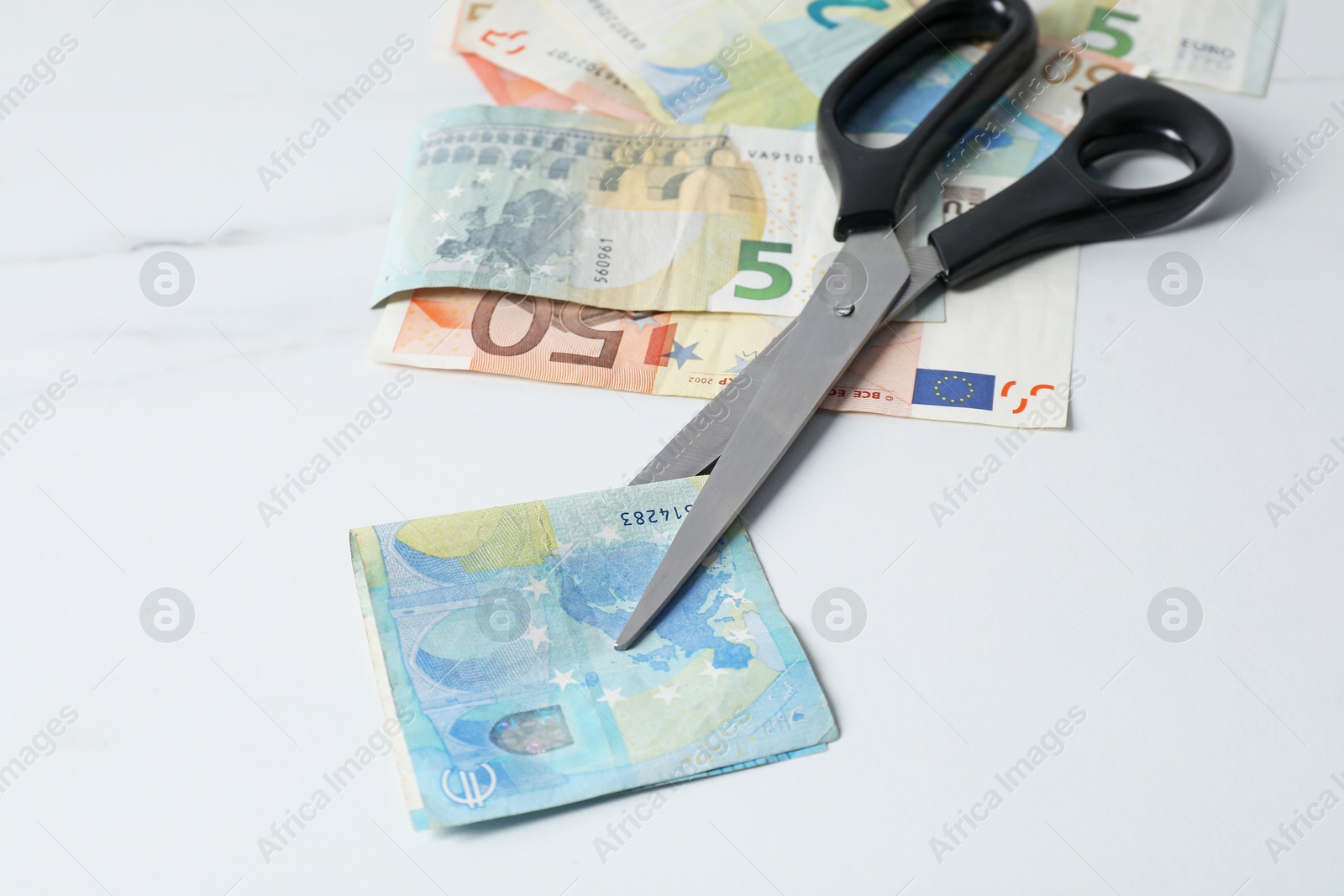 Photo of Euro banknotes and scissors on light marble table, closeup