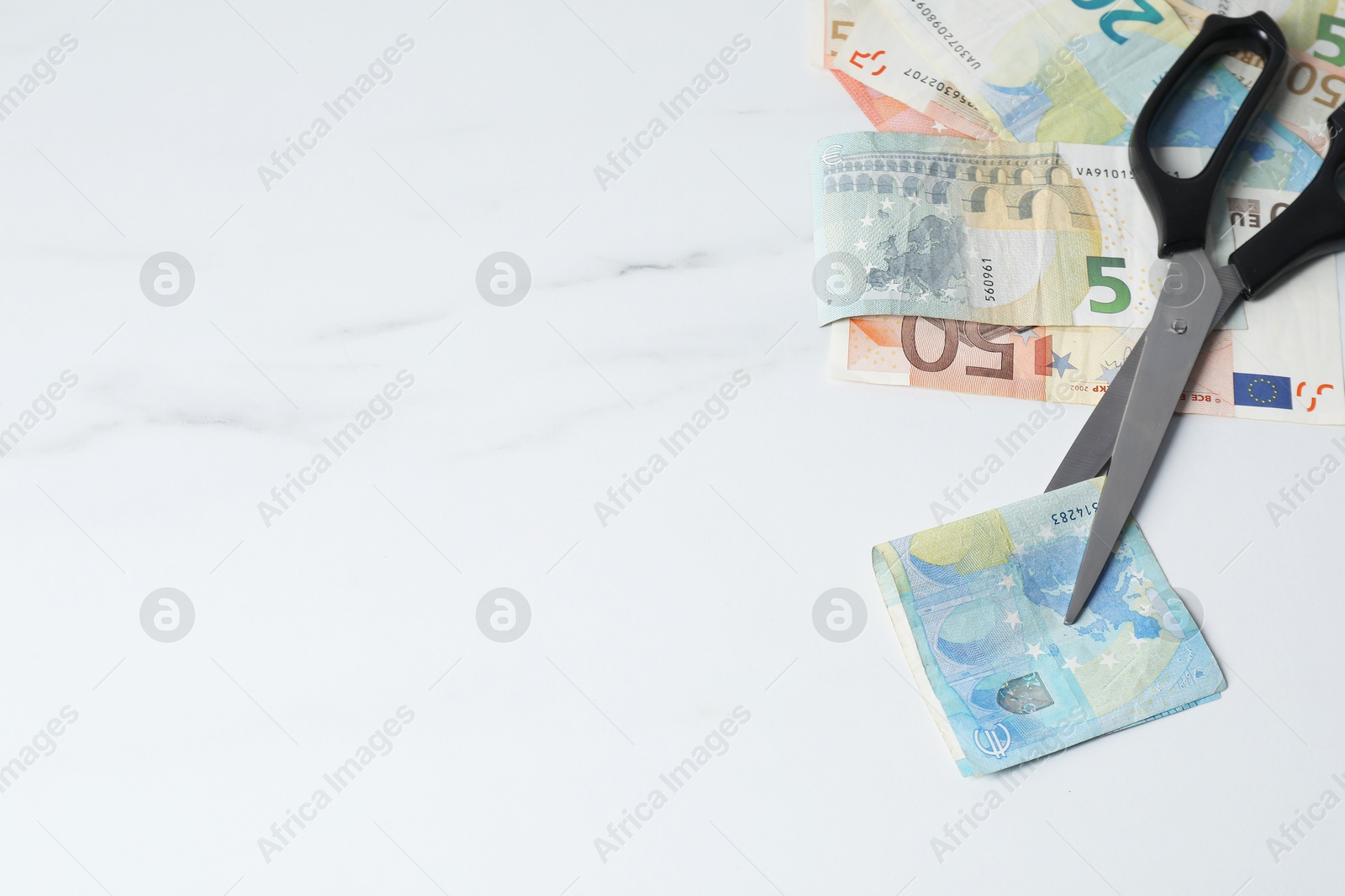 Photo of Euro banknotes and scissors on light marble table, space for text