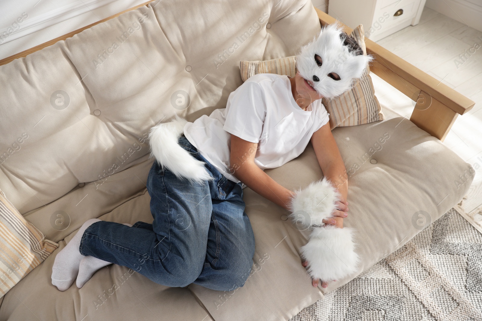 Photo of Quadrobics. Boy wearing cat mask, gloves and tail on sofa at home, above view