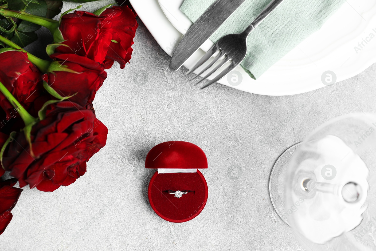 Photo of Beautiful setting for romantic dinner, engagement ring and roses on light table, flat lay