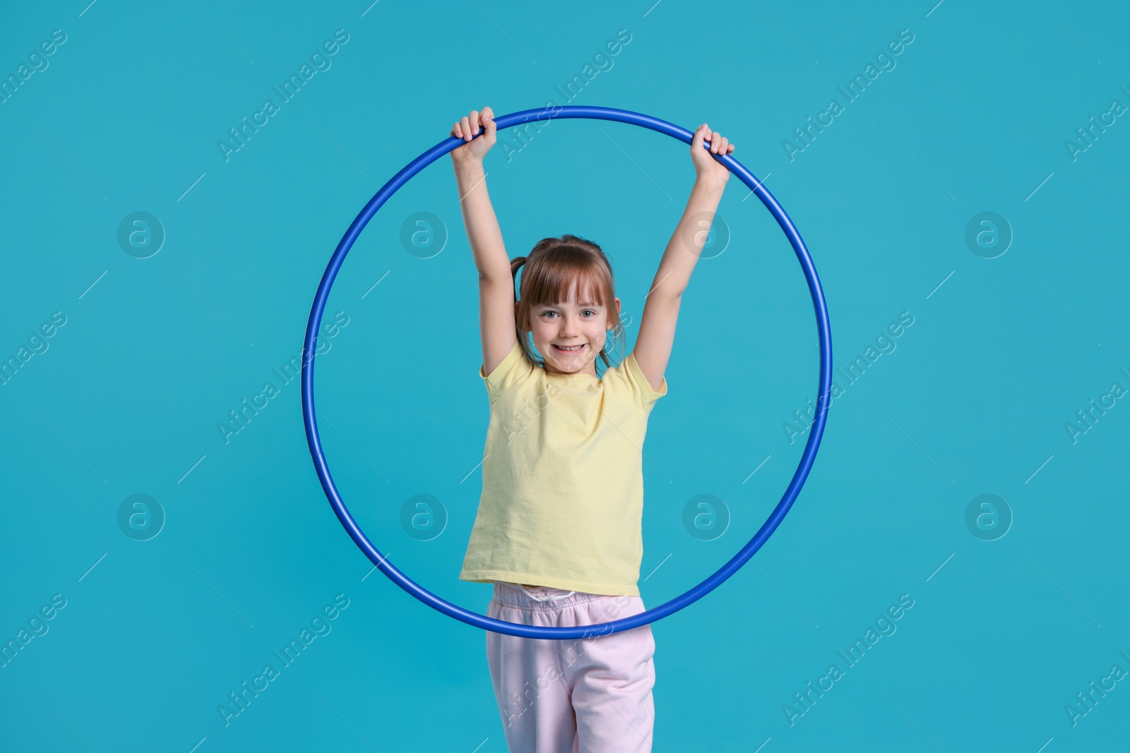 Photo of Cute little girl with hula hoop on light blue background