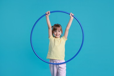 Photo of Cute little girl with hula hoop on light blue background