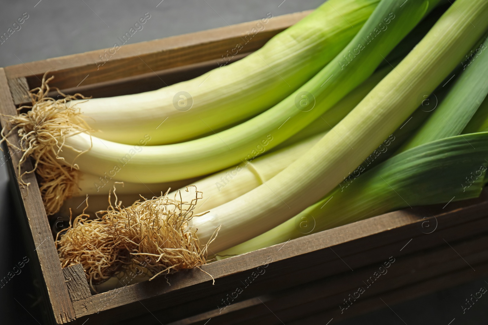 Photo of Fresh raw leeks in wooden crate on grey table, closeup