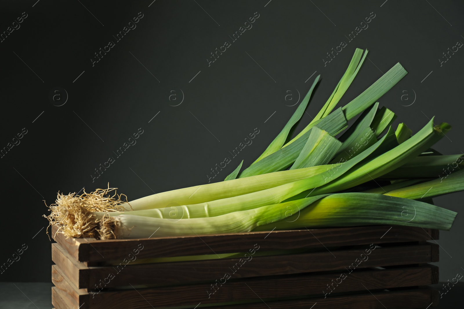 Photo of Fresh raw leeks in wooden crate on black background, closeup