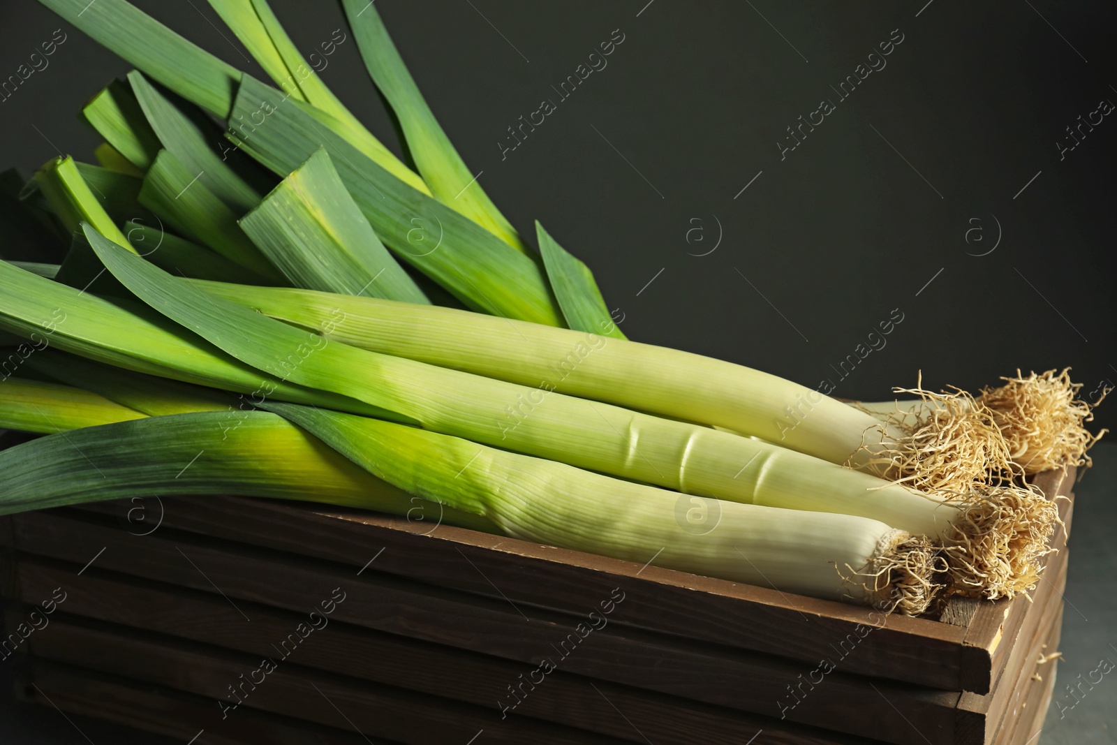 Photo of Fresh raw leeks in wooden crate on black background, closeup