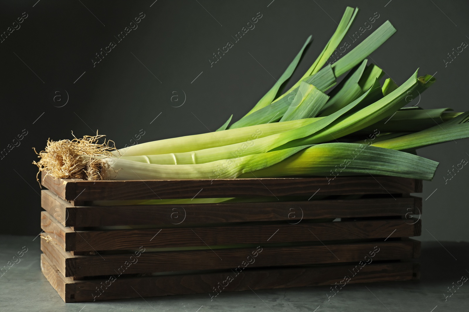 Photo of Fresh raw leeks in wooden crate on grey table, closeup