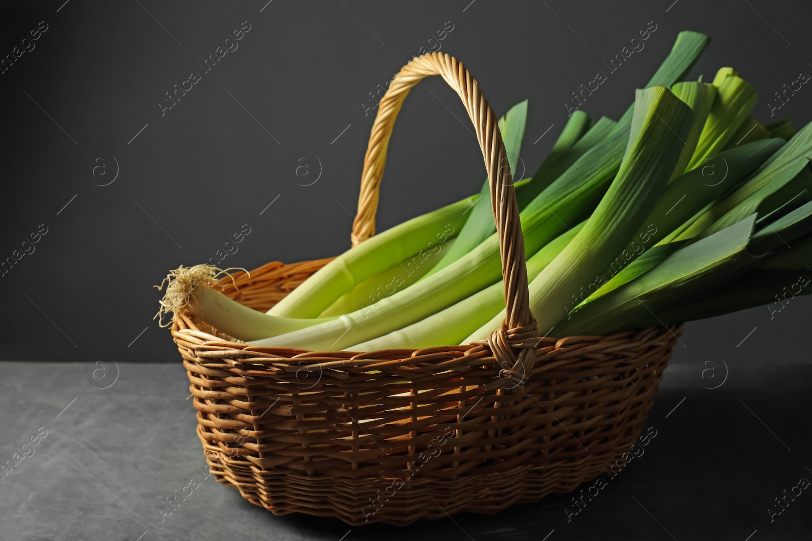 Photo of Fresh leeks in wicker basket on grey table, closeup