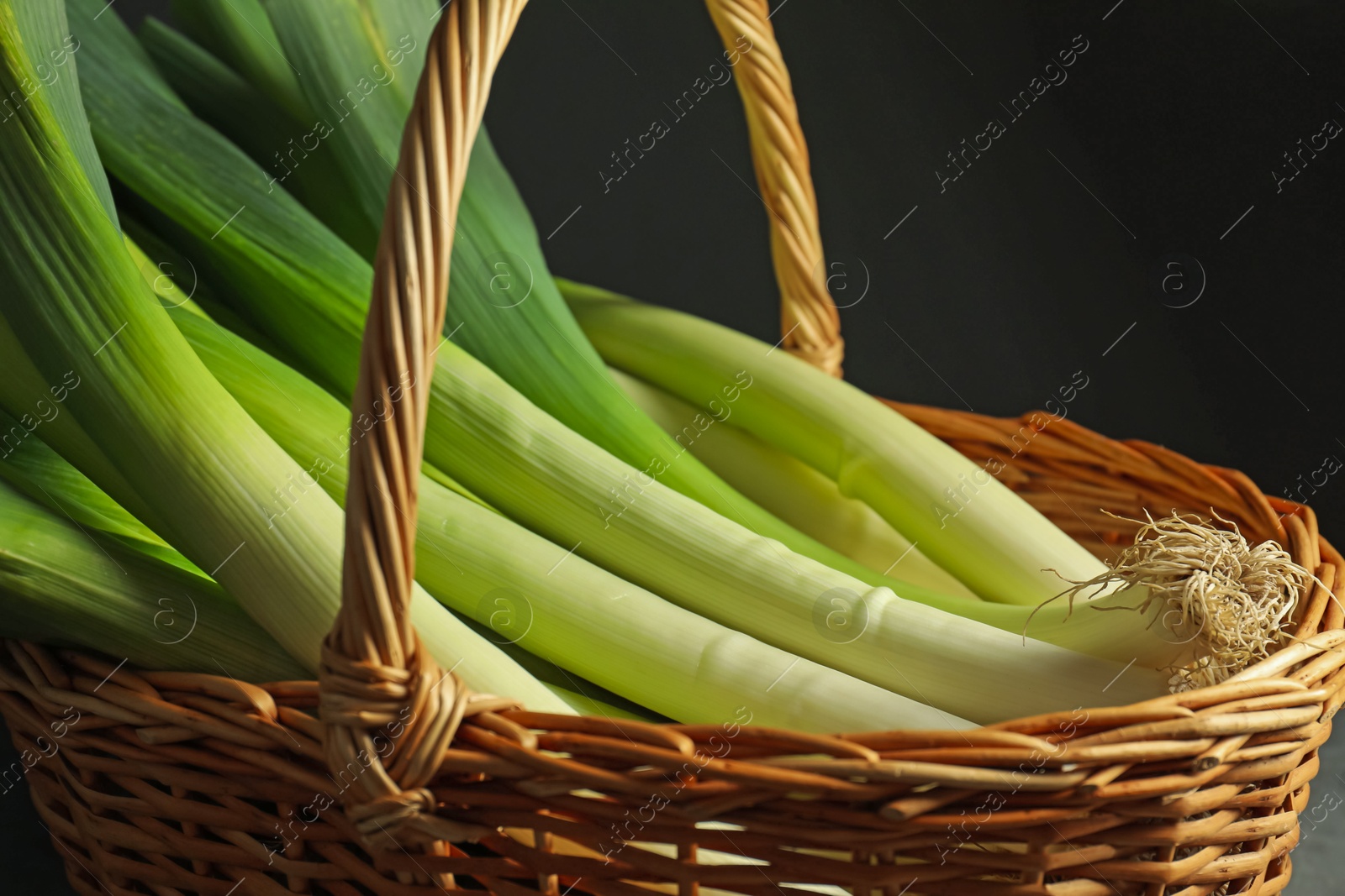 Photo of Fresh leeks in wicker basket on black background, closeup