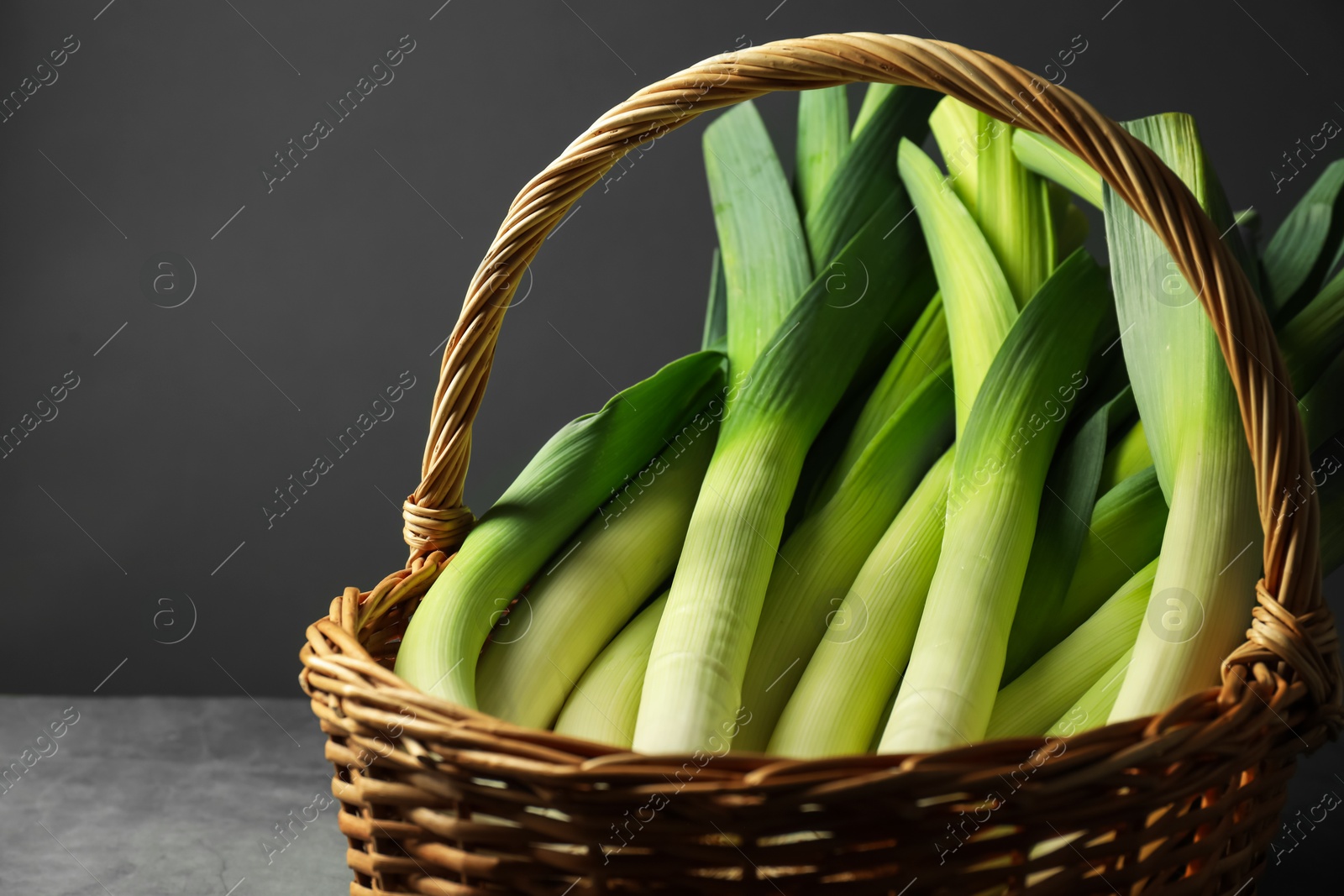 Photo of Fresh leeks in wicker basket on grey table, closeup