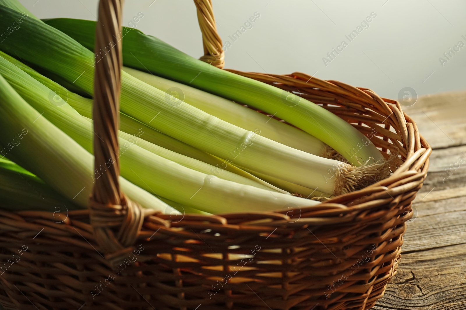 Photo of Fresh leeks in wicker basket on wooden table, closeup