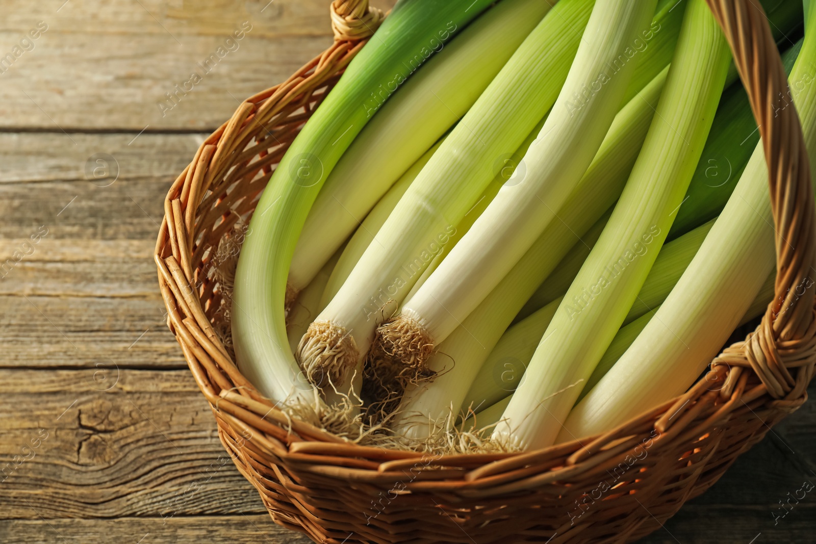 Photo of Fresh leeks in wicker basket on wooden table, closeup