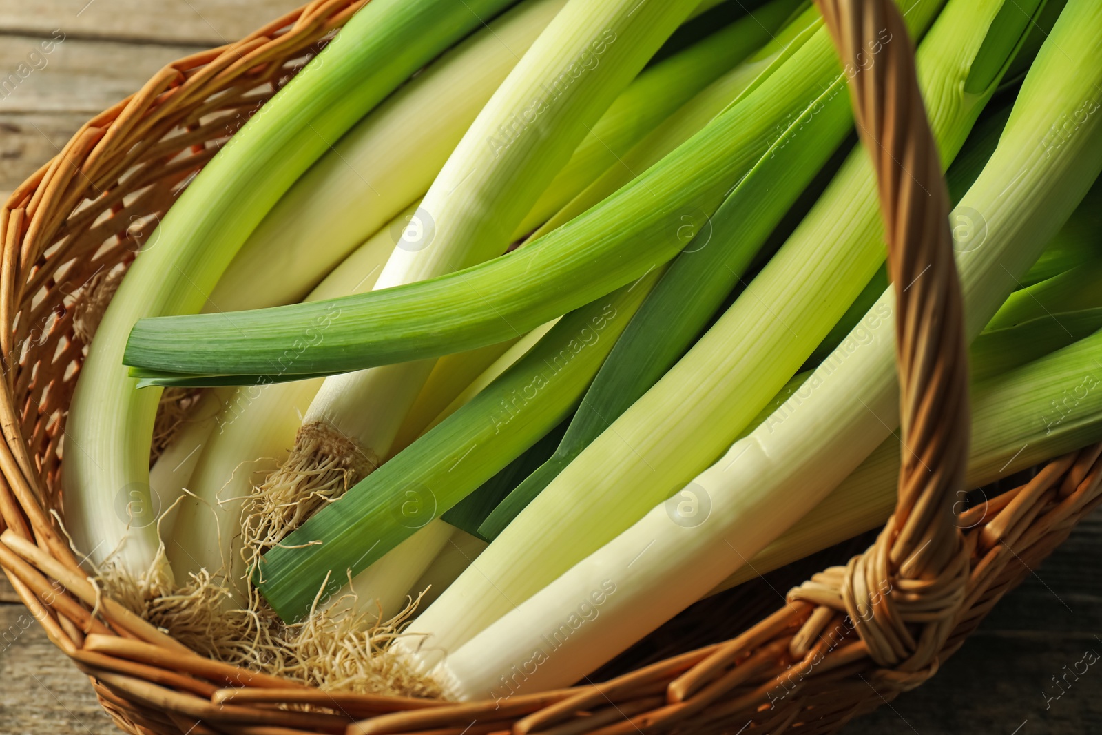 Photo of Fresh leeks in wicker basket on wooden table, closeup