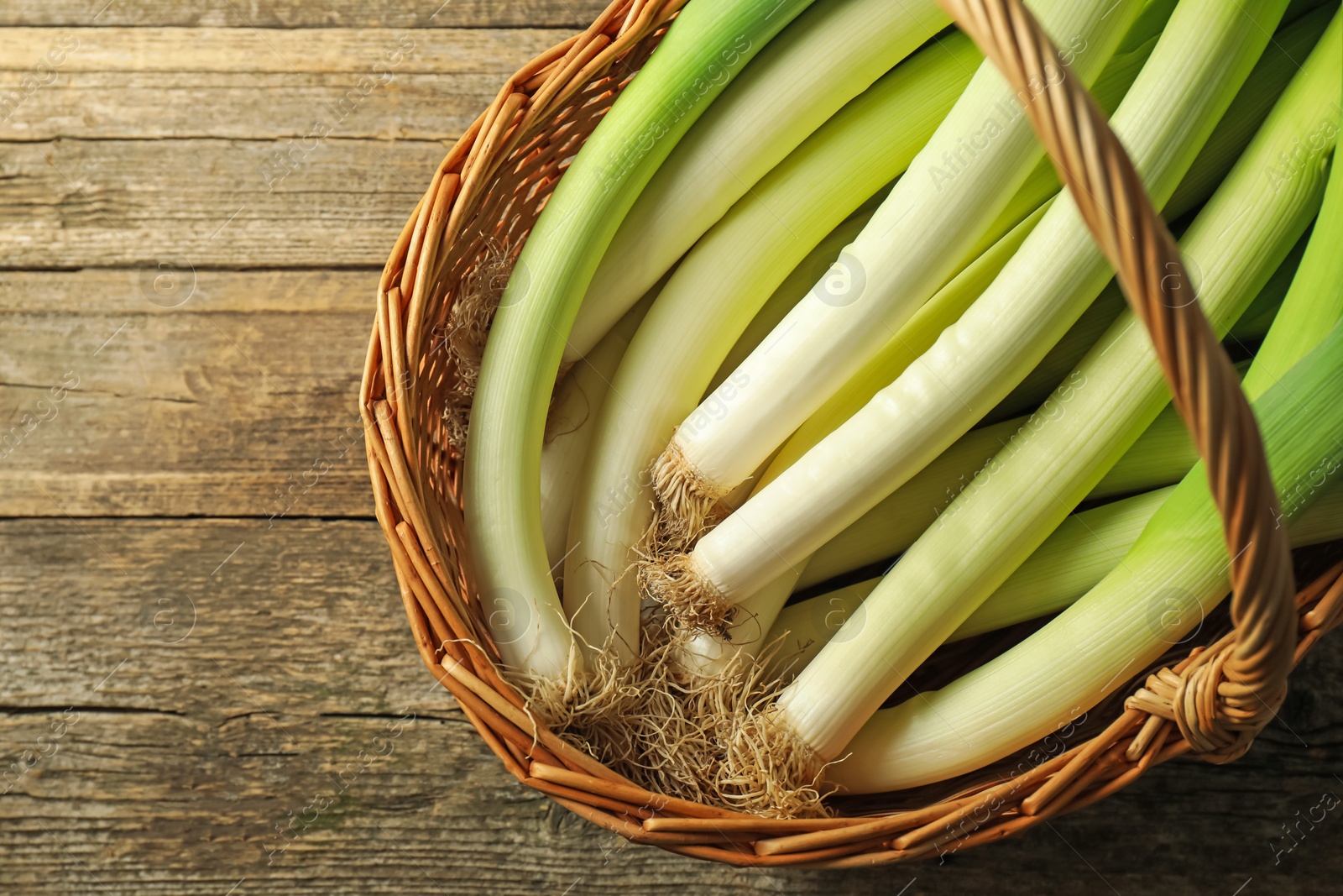 Photo of Fresh leeks in wicker basket on wooden table, top view