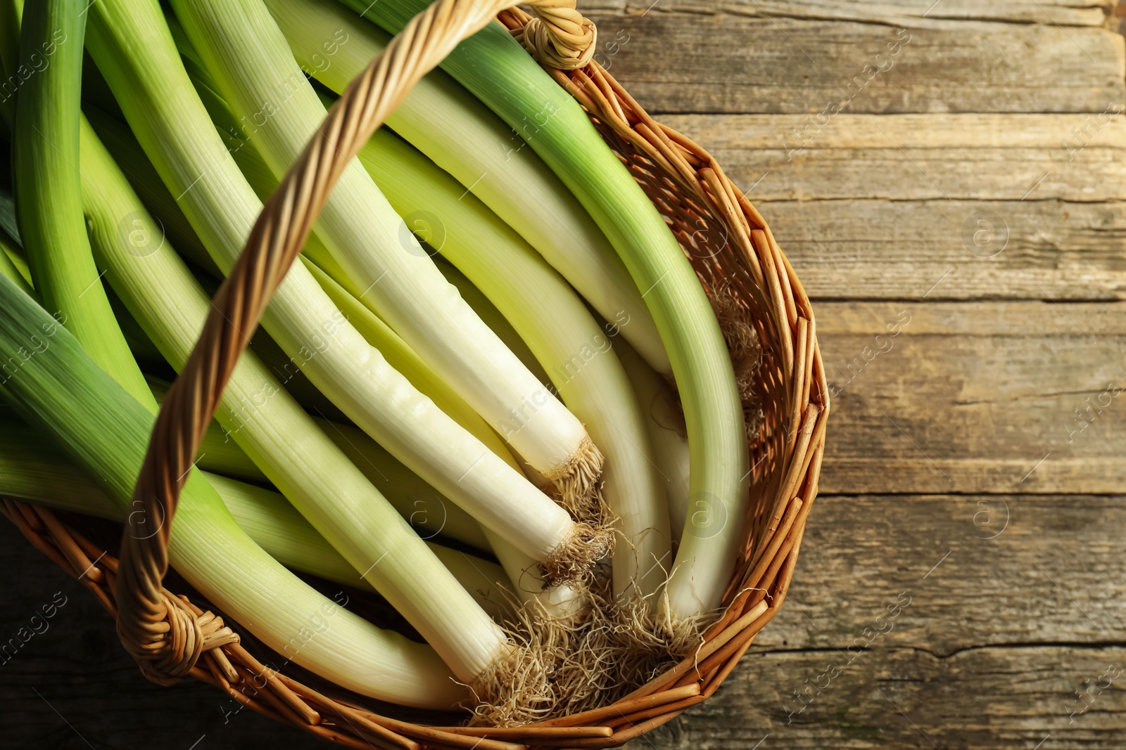 Photo of Fresh leeks in wicker basket on wooden table, top view