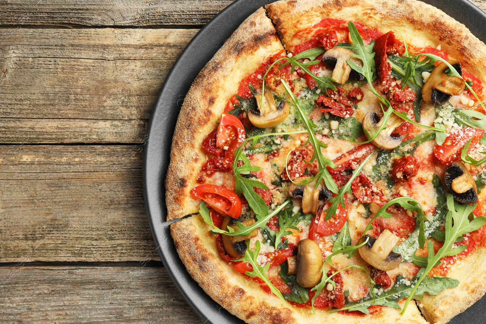 Photo of Tasty pizza with mushrooms, tomatoes and arugula on wooden table, top view. Space for text