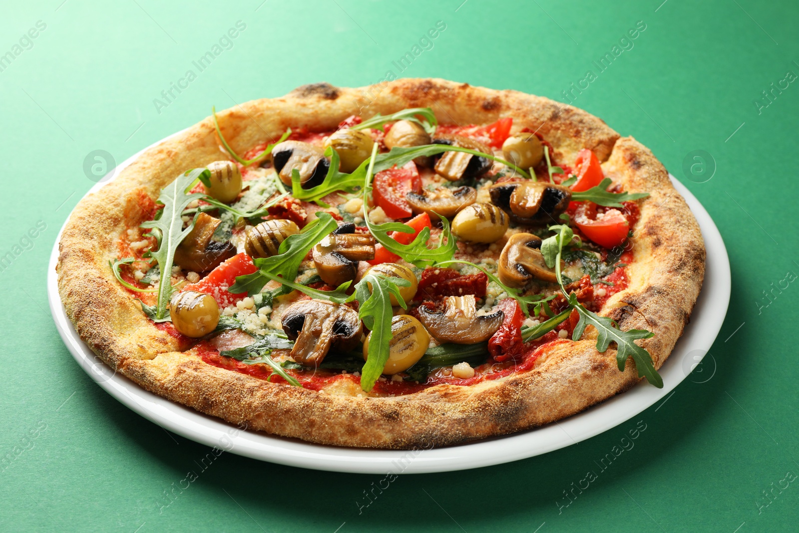 Photo of Tasty pizza with mushrooms, olives and arugula on green background, closeup