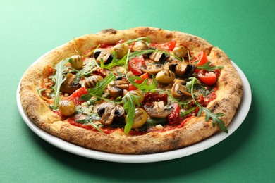 Tasty pizza with mushrooms, olives and arugula on green background, closeup