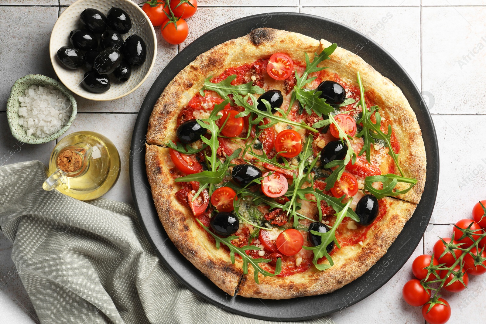 Photo of Tasty pizza with black olives, tomatoes and arugula served on light tiled table, flat lay