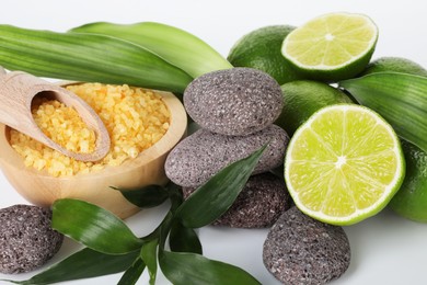 Photo of Spa composition with limes, massage stones, sea salt and green leaves on white background, closeup