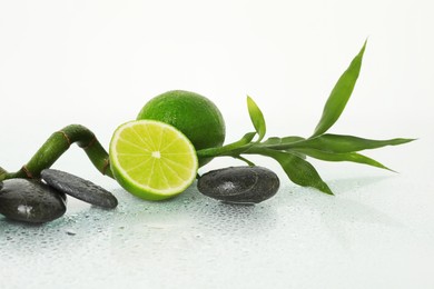 Photo of Spa composition with limes, massage stones and bamboo stem on wet surface against white background