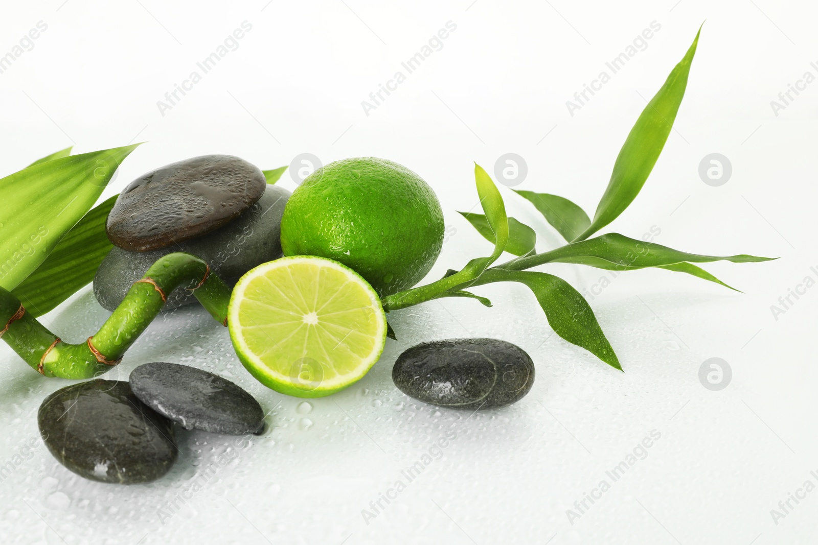 Spa composition with limes, massage stones and bamboo stem on wet surface Photo of Spa composition with limes, massage stones and bamboo stem on wet surface