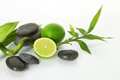 Photo of Spa composition with limes, massage stones and bamboo stem on wet surface