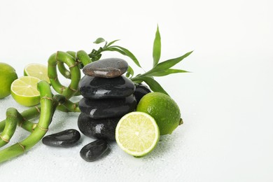 Photo of Spa composition with limes, massage stones and bamboo stems on wet surface against white background, space for text