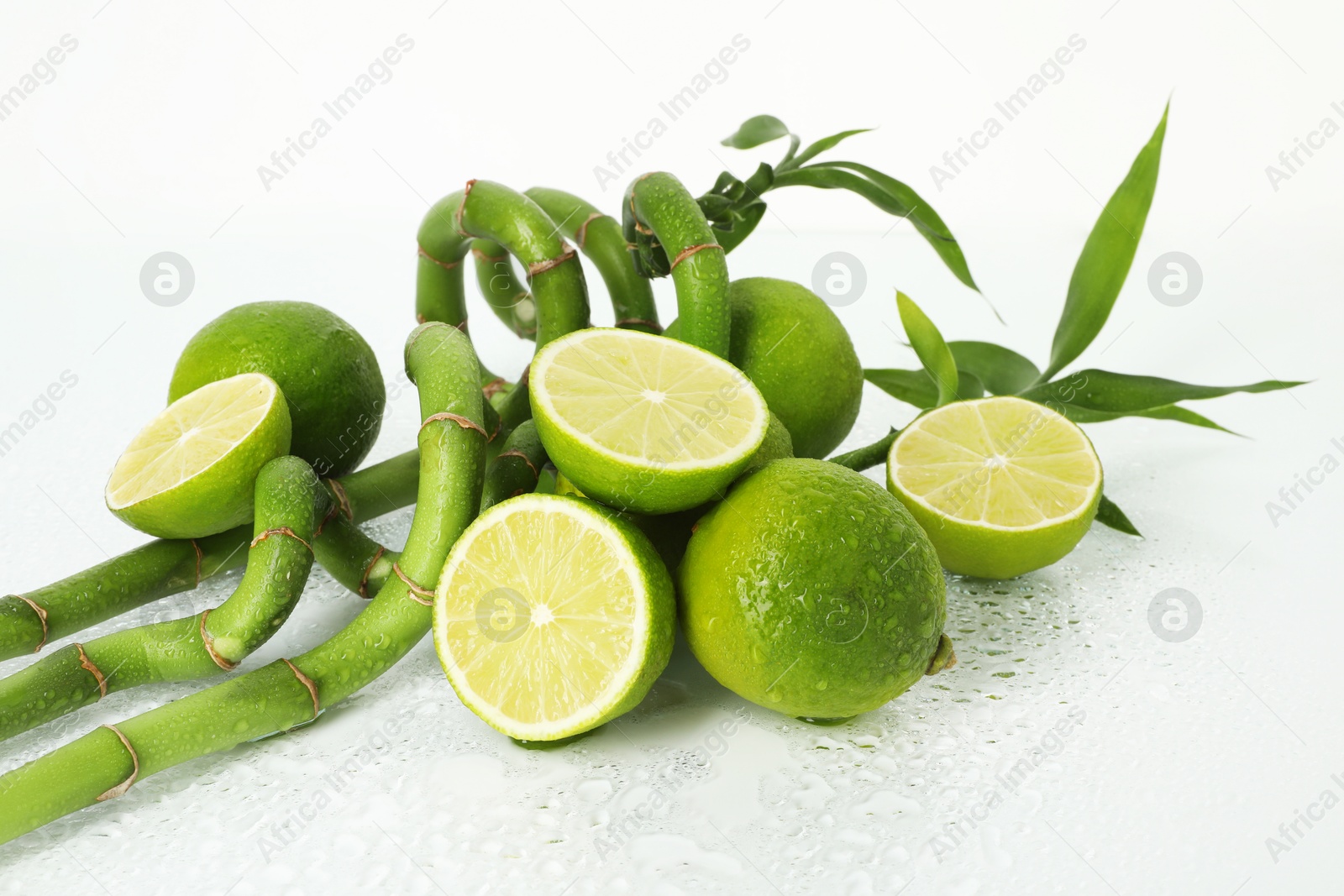 Fresh limes and bamboo stems on wet surface against white background Photo of Fresh limes and bamboo stems on wet surface against white background