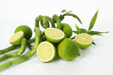 Photo of Fresh limes and bamboo stems on wet surface against white background