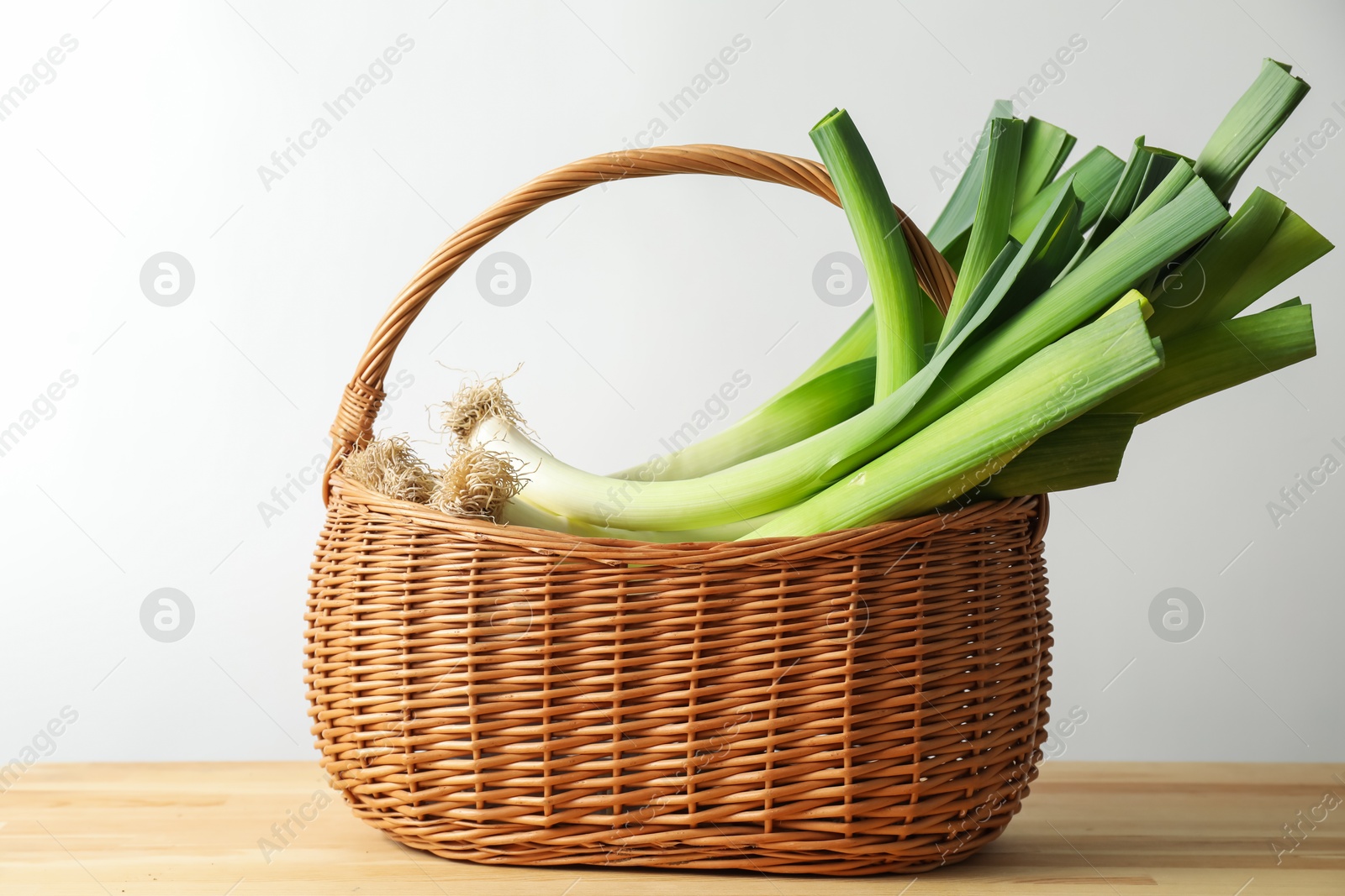 Photo of Fresh leeks in basket on wooden table