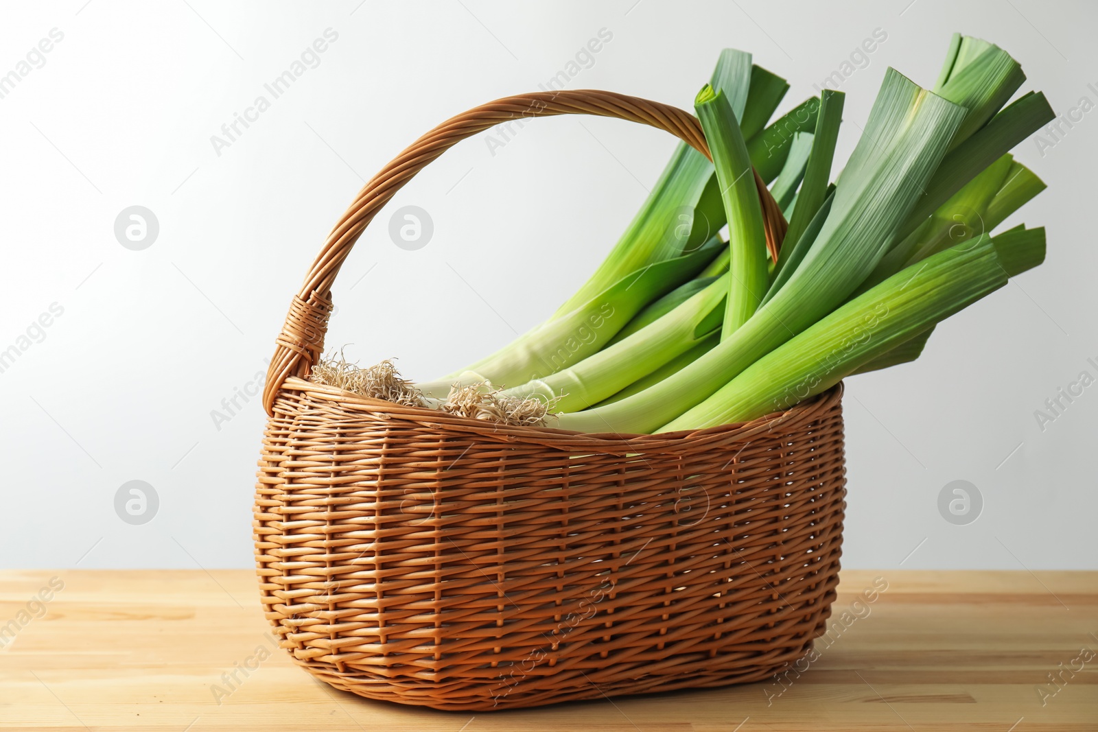 Photo of Fresh leeks in basket on wooden table