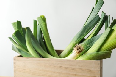 Photo of Fresh leeks in wooden crate on light background, closeup