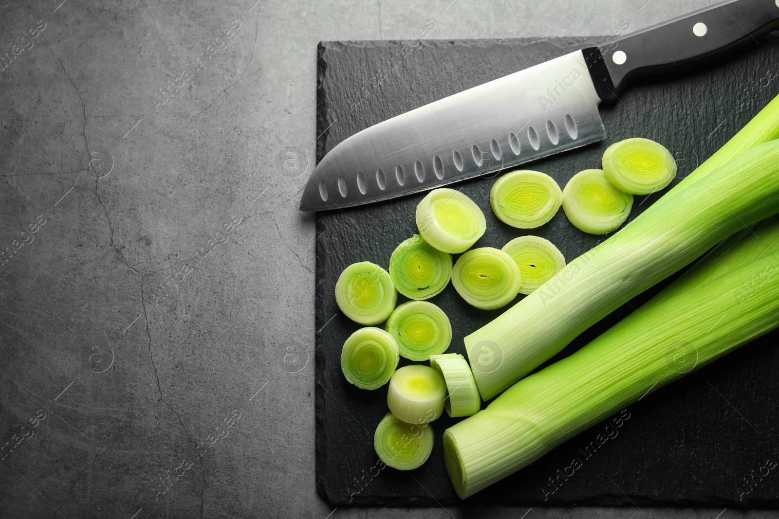 Photo of Chopped leeks and knife on grey table, top view. Space for text