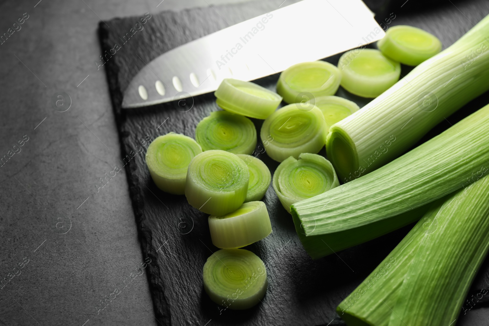 Photo of Chopped leeks and knife on grey table, closeup