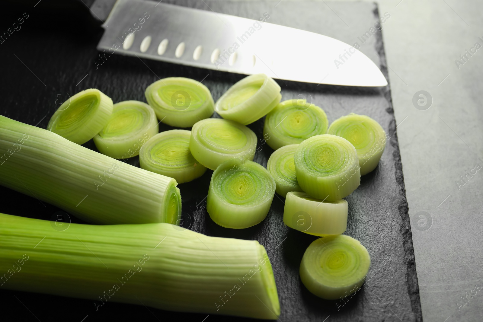 Photo of Chopped leeks and knife on grey table, closeup