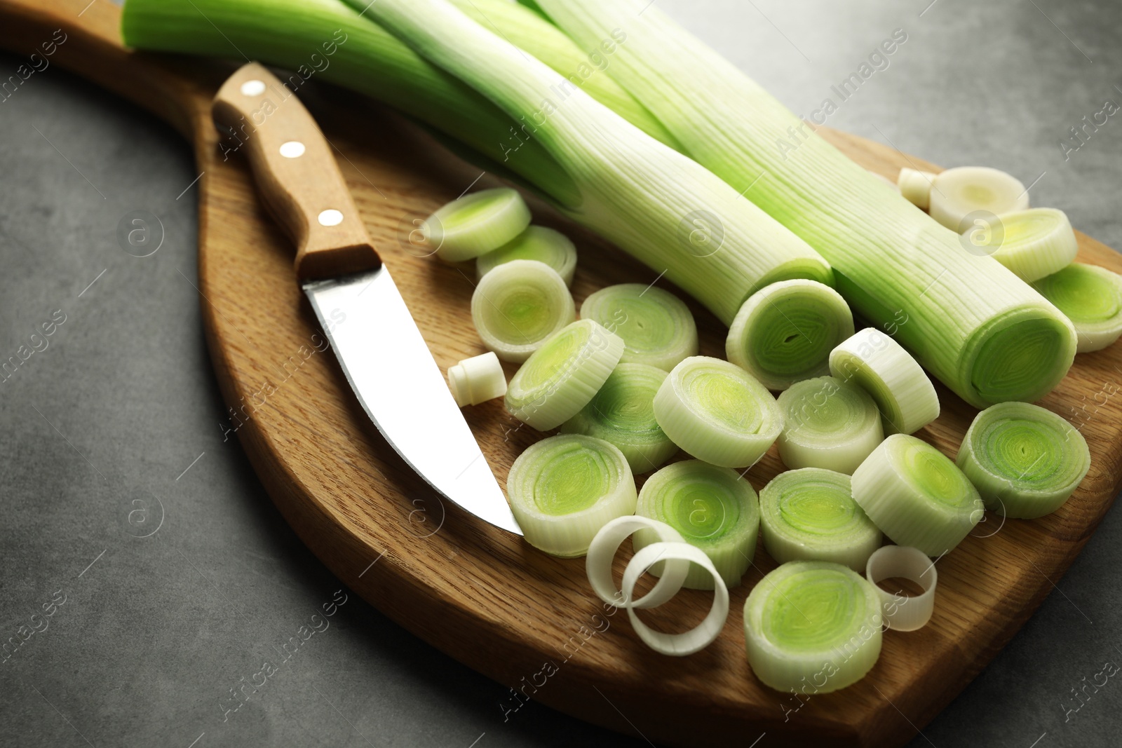 Photo of Chopped leeks and knife on grey table, closeup