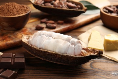 Photo of Cocoa pod with beans, chocolate and butter on wooden table, closeup