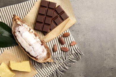 Photo of Cocoa pod with beans, butter and chocolate on grey table, flat lay. Space for text