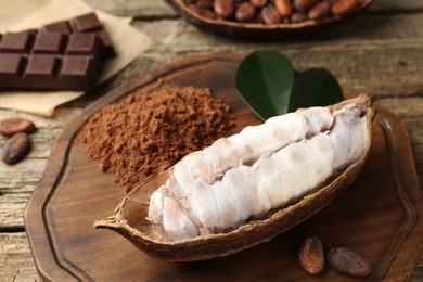 Photo of Cocoa pod with beans, powder and chocolate on wooden table, closeup