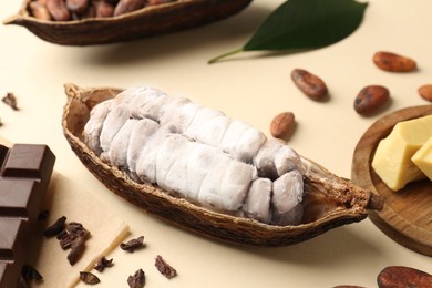 Photo of Cocoa pod with beans, butter and chocolate on beige background, closeup