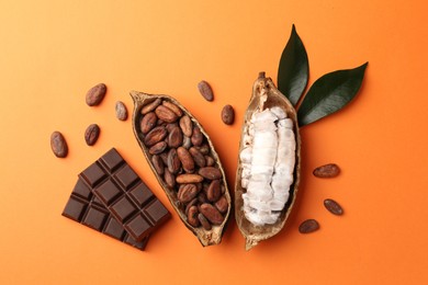 Photo of Cocoa pods with beans and chocolate on orange background, flat lay