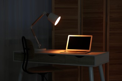 Photo of Comfortable workplace with laptop and lamp on table indoors