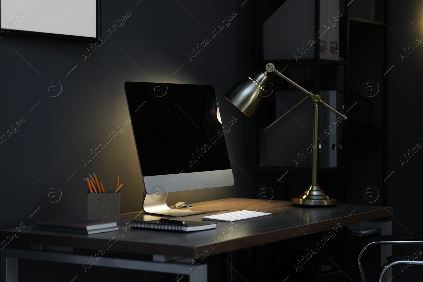 Comfortable workplace with computer and lamp on wooden desk at home office in evening Photo of Comfortable workplace with computer and lamp on wooden desk at home office in evening