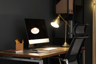 Photo of Comfortable workplace with computer and lamp on wooden desk in home office