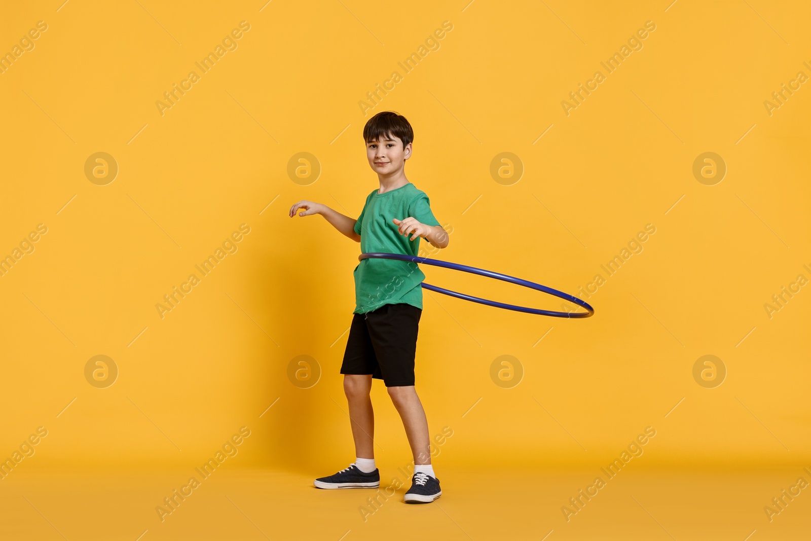 Photo of Boy exercising with hula hoop on yellow background